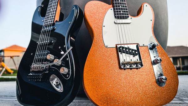 Two custom guitars built by JTal Guitars in Elkhorn, NE. One Telecaster style guitar is orange with metallic flake, the other is a Super Strat style all black